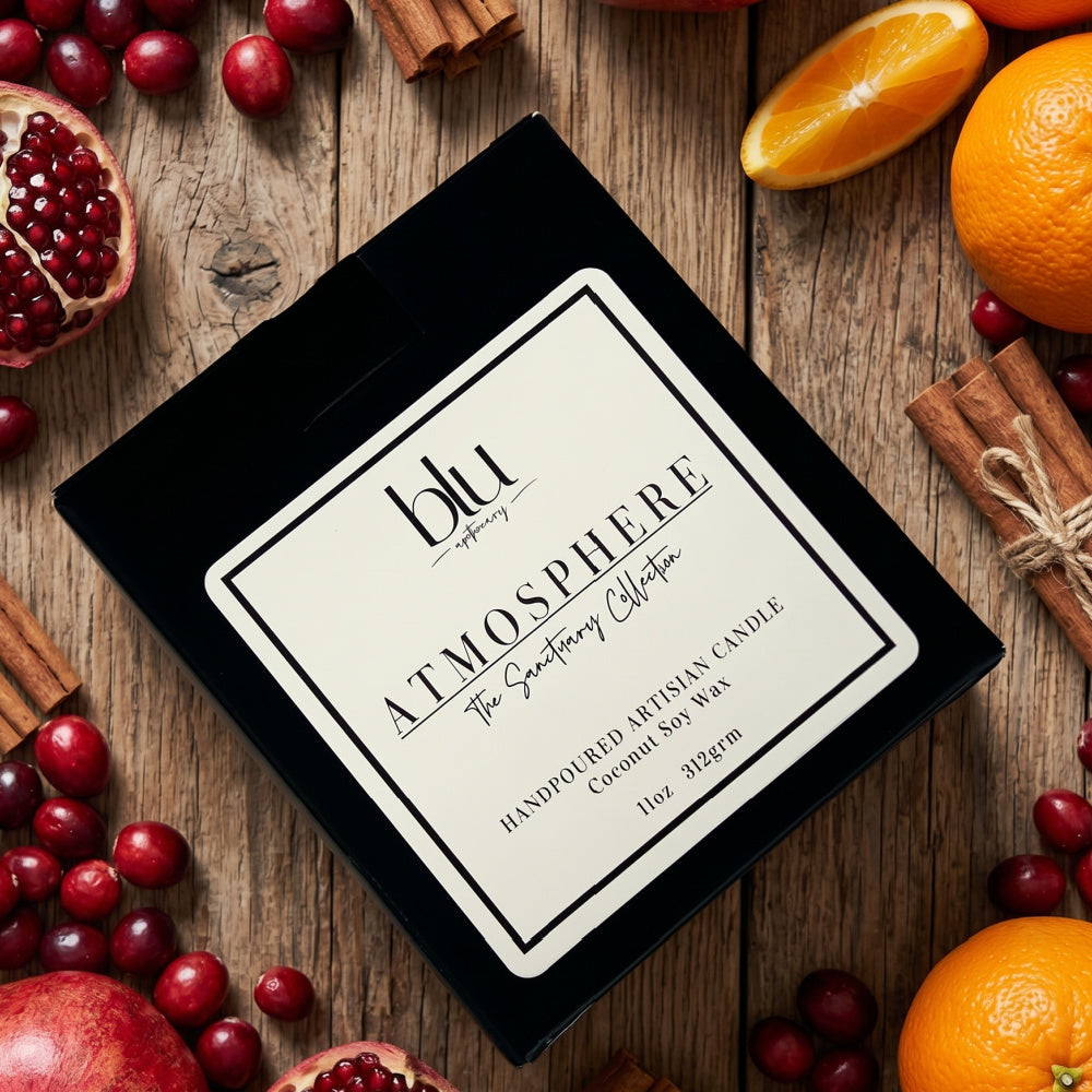 Atmosphere by BLU Gather artisan candle black gift box flat lay on rustic wood table styled with fresh cranberries, pomegranates, orange slices, and cinnamon sticks