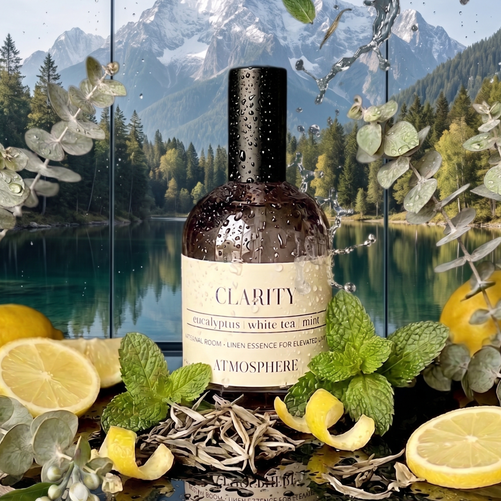 A bottle of Clarity Aromatherapy essential oil in eucalyptus and white tea mint scent, styled with fresh mint leaves, lemon slices, and dried botanicals in front of a scenic mountain lake background. eucalyptus room mist