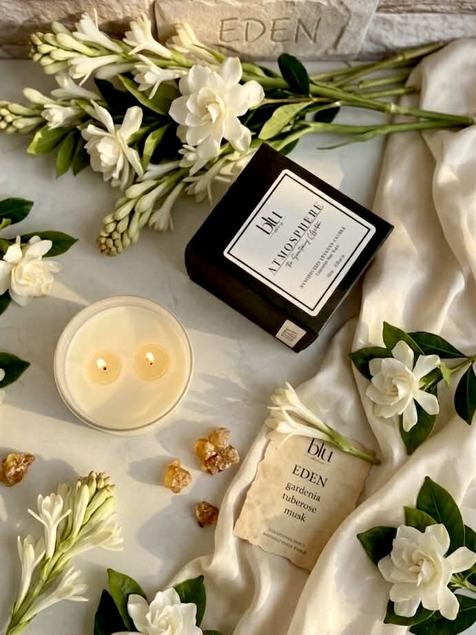 Candle, bottle, and flowers with 'Eden' branding on a textured surface tuberose candle, peony candle, gardenia candle