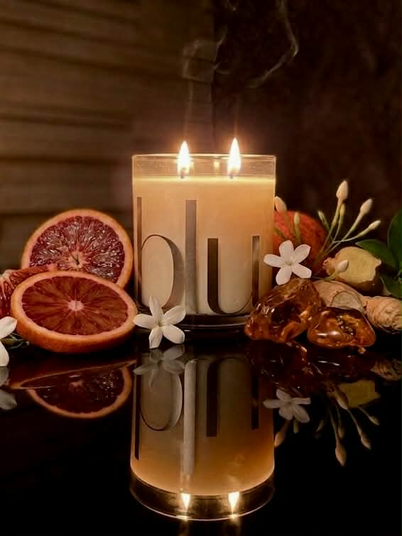 Candle with decorative fruits and flowers on a reflective surface