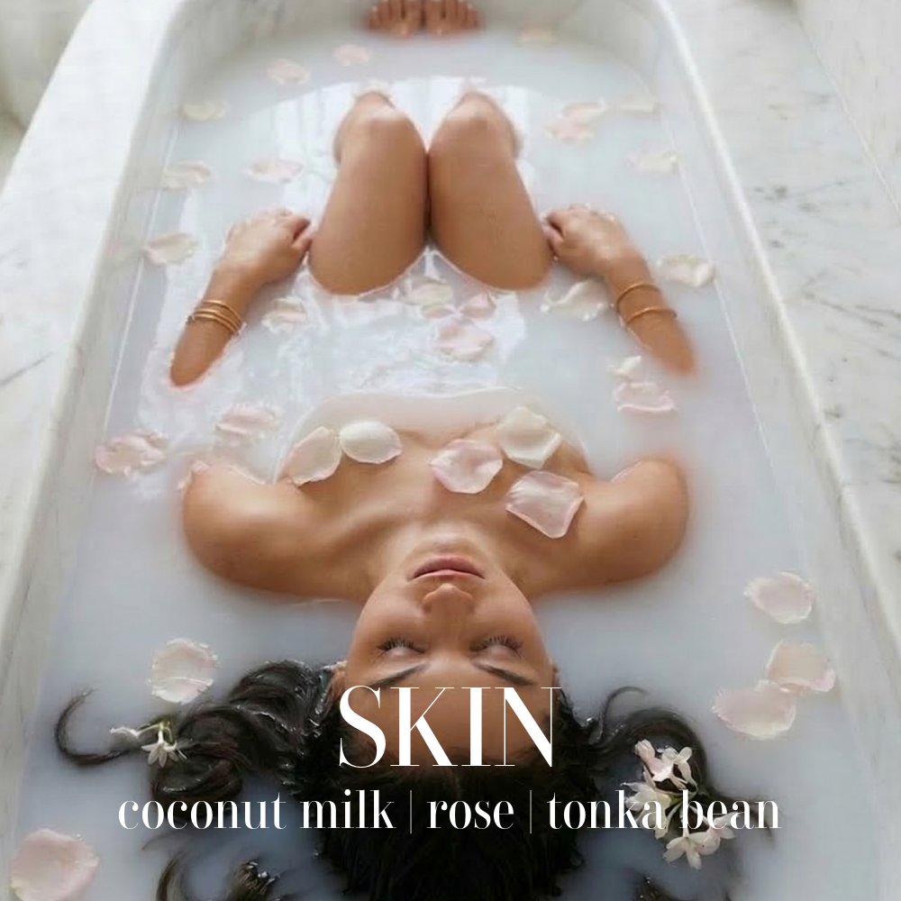 A serene woman submerged in a milky bath with pink rose petals, representing the Skin artisan candle from the Sanctuary Collection