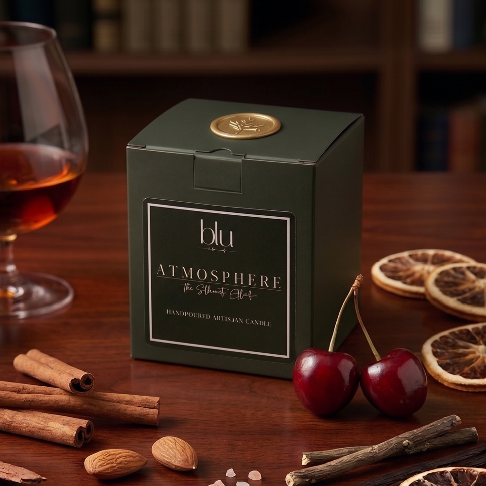 Green 'blu Atmosphere' candle box on a wooden table with cherries, cinnamon sticks, and dried oranges.
