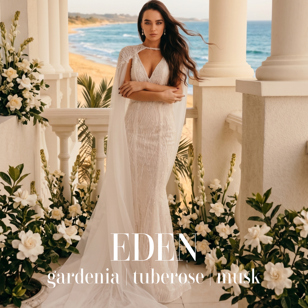 Woman in a white dress standing on a balcony with flowers and ocean view, featuring the brand 'Eden'. Eden artisan candle