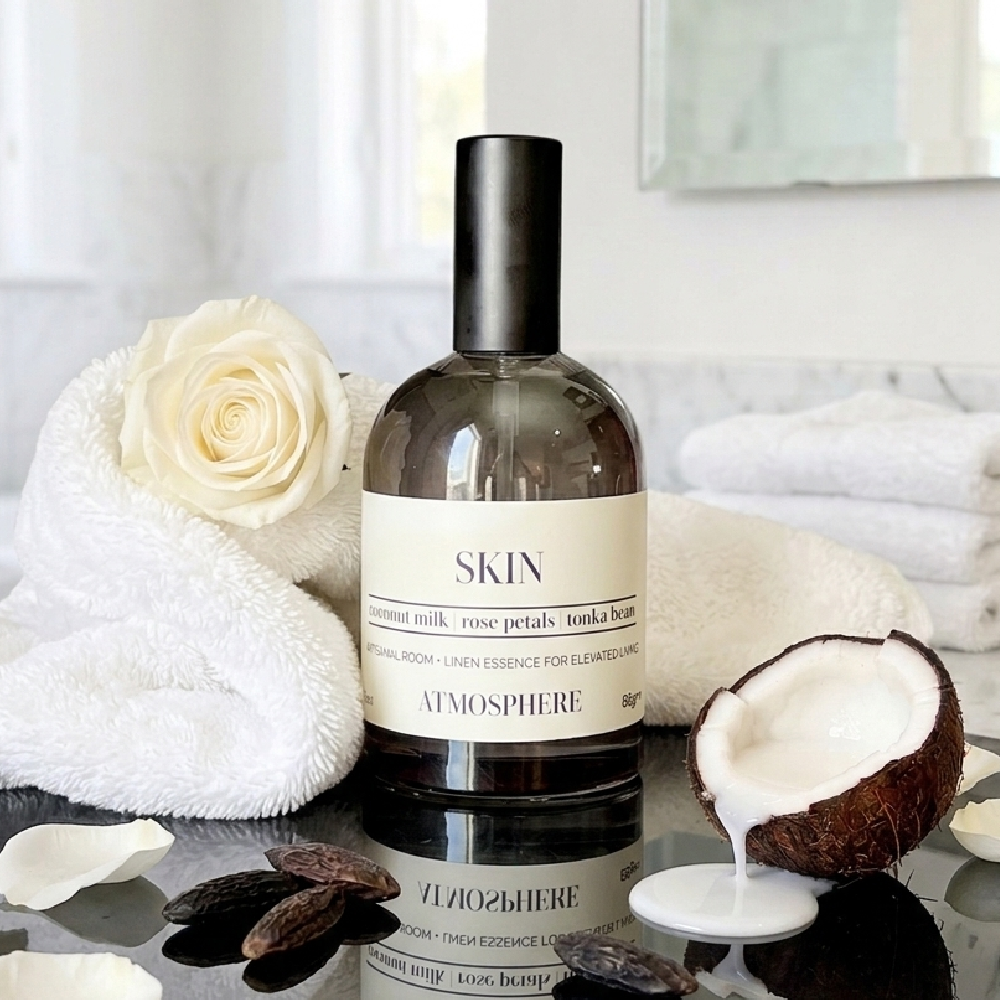 A bottle of ATMOSPHERE Skincare 'Rose Petals' body wash, styled with white towels, a white rose, and a halved coconut on a reflective dark surface. coconut rose linen mist