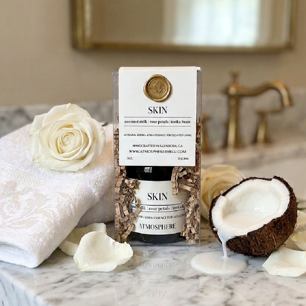 A boxed skincare product labeled SKIN stands on a marble surface with a white towel, white roses, and a halved coconut nearby. The setting is a styled bathroom-like scene with a mirror and brass faucet in the background, so this is Lifestyle rather than Product/Packaging because a real environment is present. Skin Room Spray